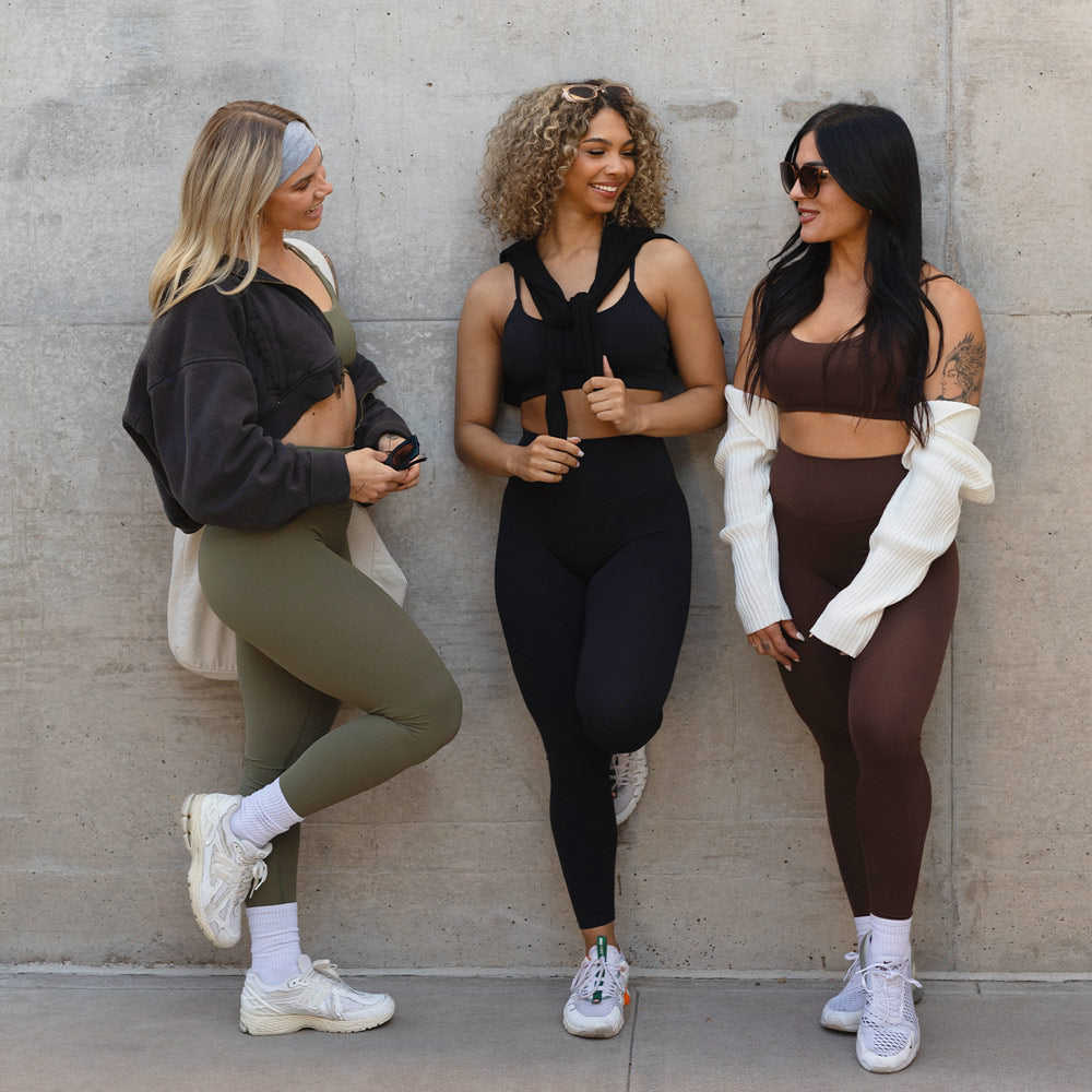 Three women in activewear chatting against a concrete wall.